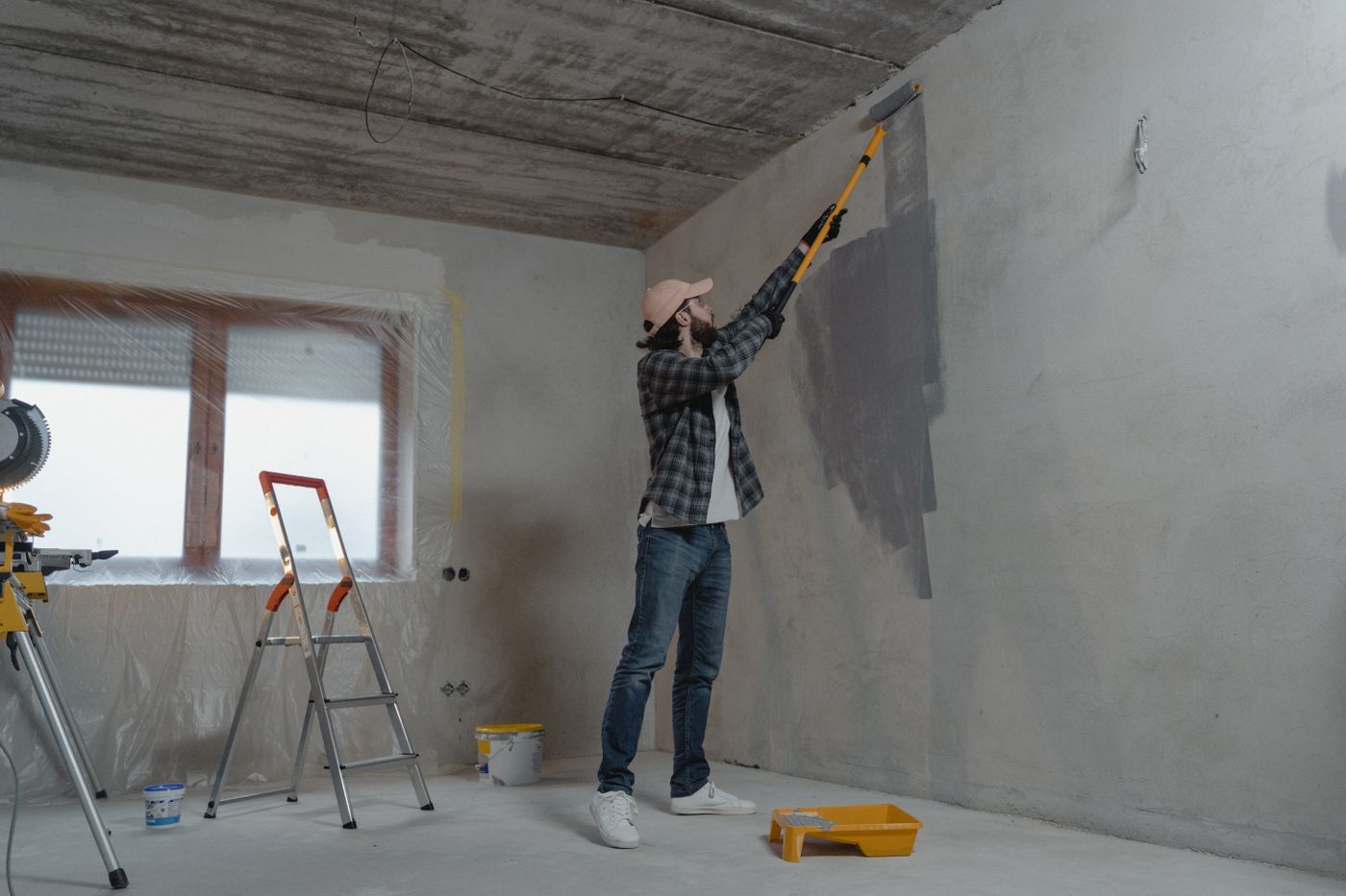 Man verft een grijze muur in een kale ruimte met een verfroller op een lange steel
